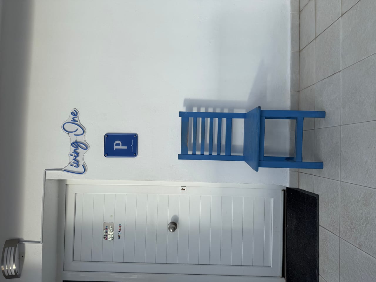 Entrada de Living One con rótulo y silla azul mediterránea, la personalidad de la marca