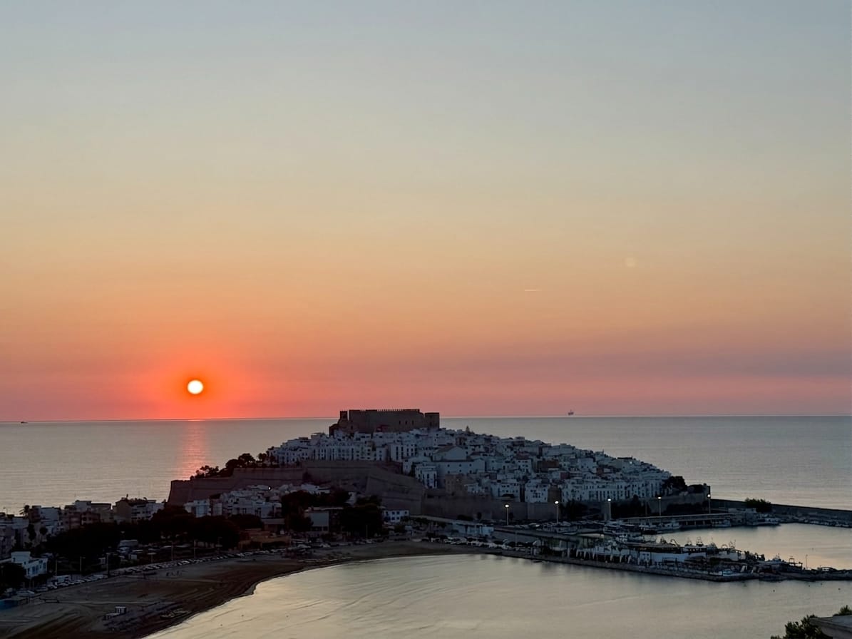 Atardecer sobre el mar con el sol cayendo junto al castillo de Peñíscola y la bahía en calma