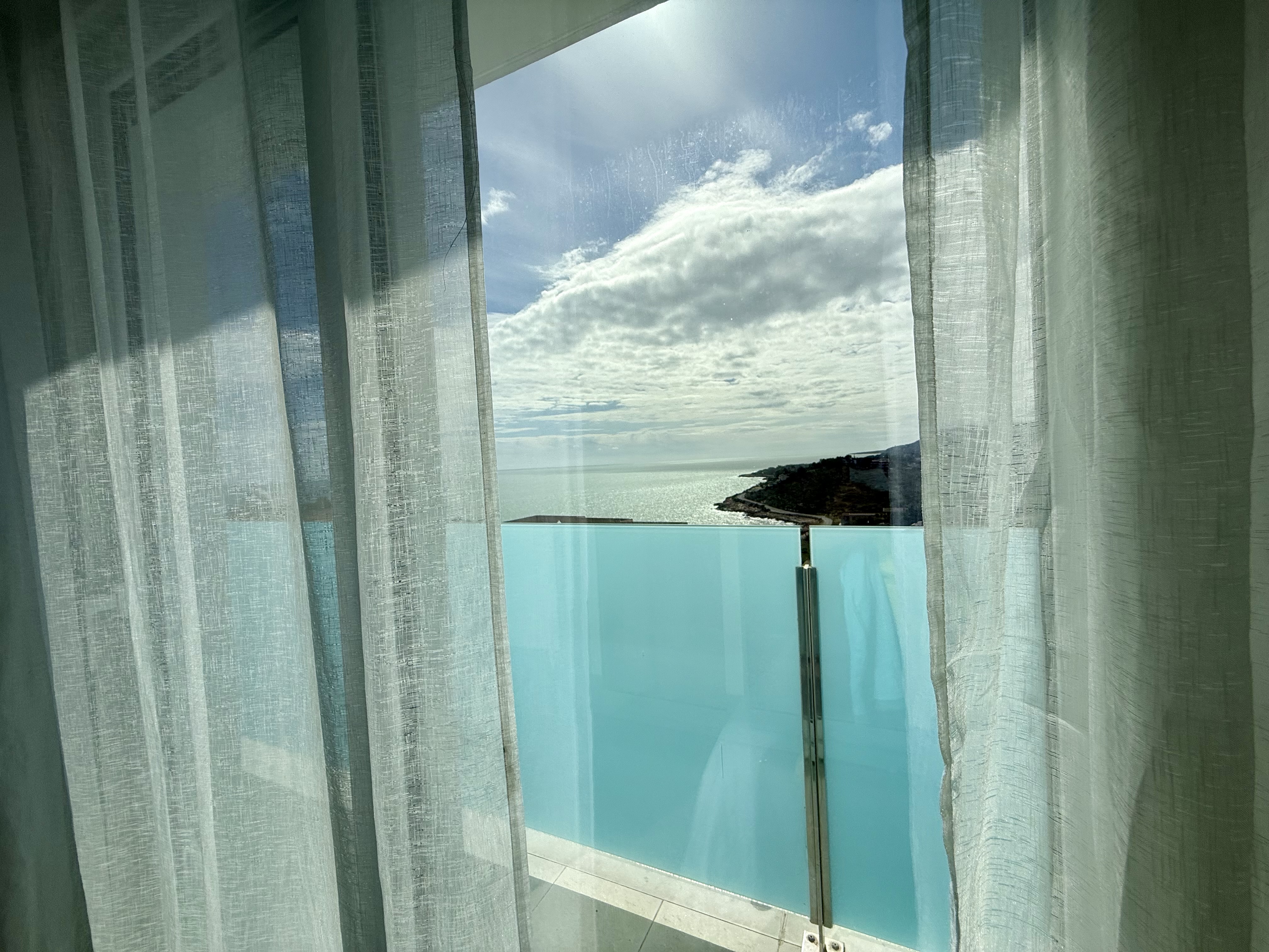 Mar enmarcado por cortinas de lino y barandilla de cristal turquesa desde la terraza de Living One