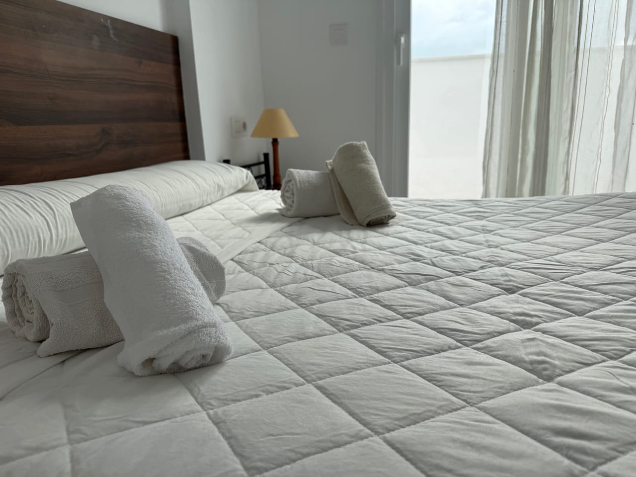 Detalle de cama con toallas enrolladas y lámpara, cada detalle cuenta