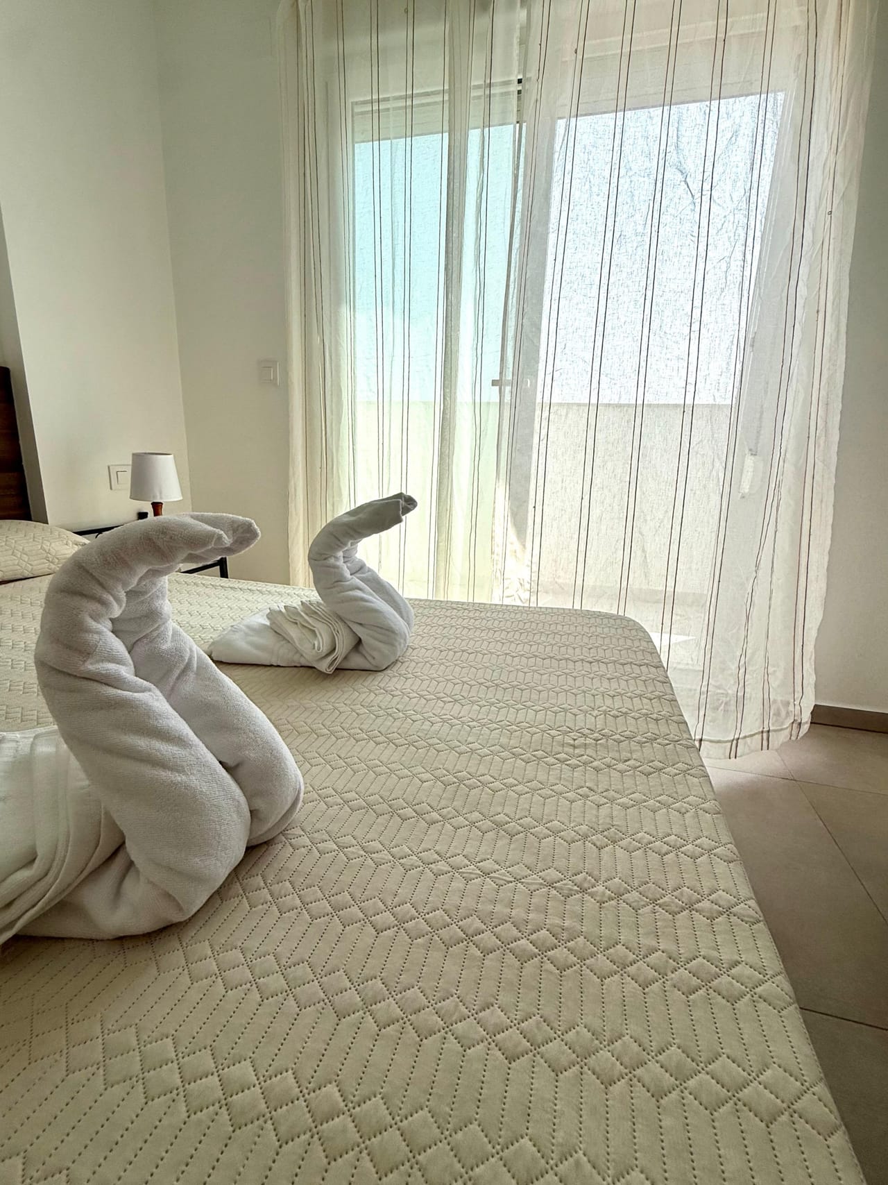 Toallas dobladas con forma de cisne sobre la cama, junto a la terraza con vistas al mar