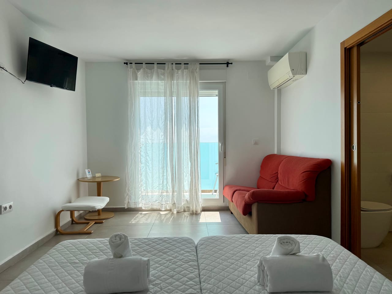 Habitación con camas, cortinas de lino y salida a la terraza con vistas al mar Mediterráneo