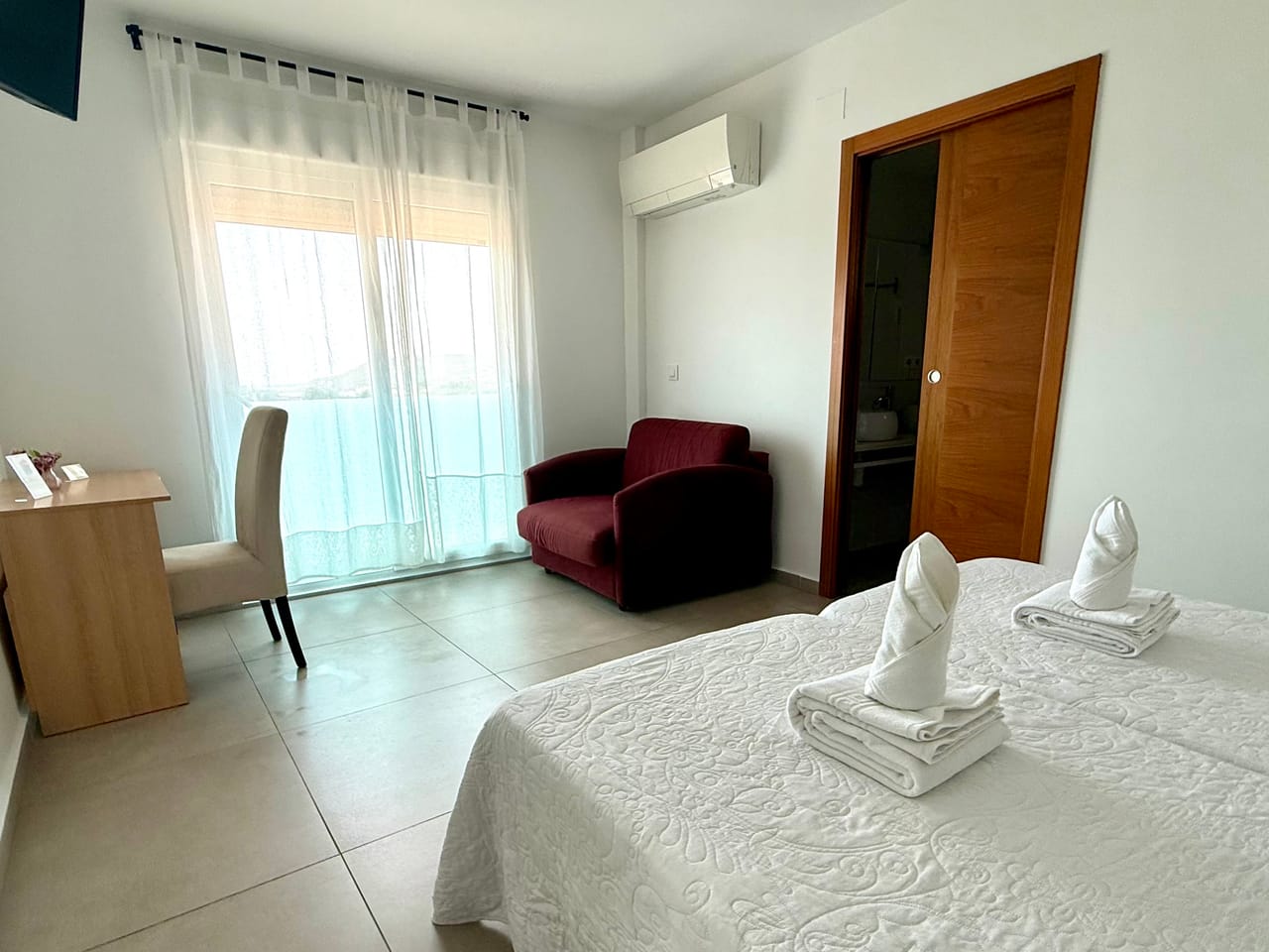 Habitación con sillón burdeos, escritorio y vistas al mar por la terraza