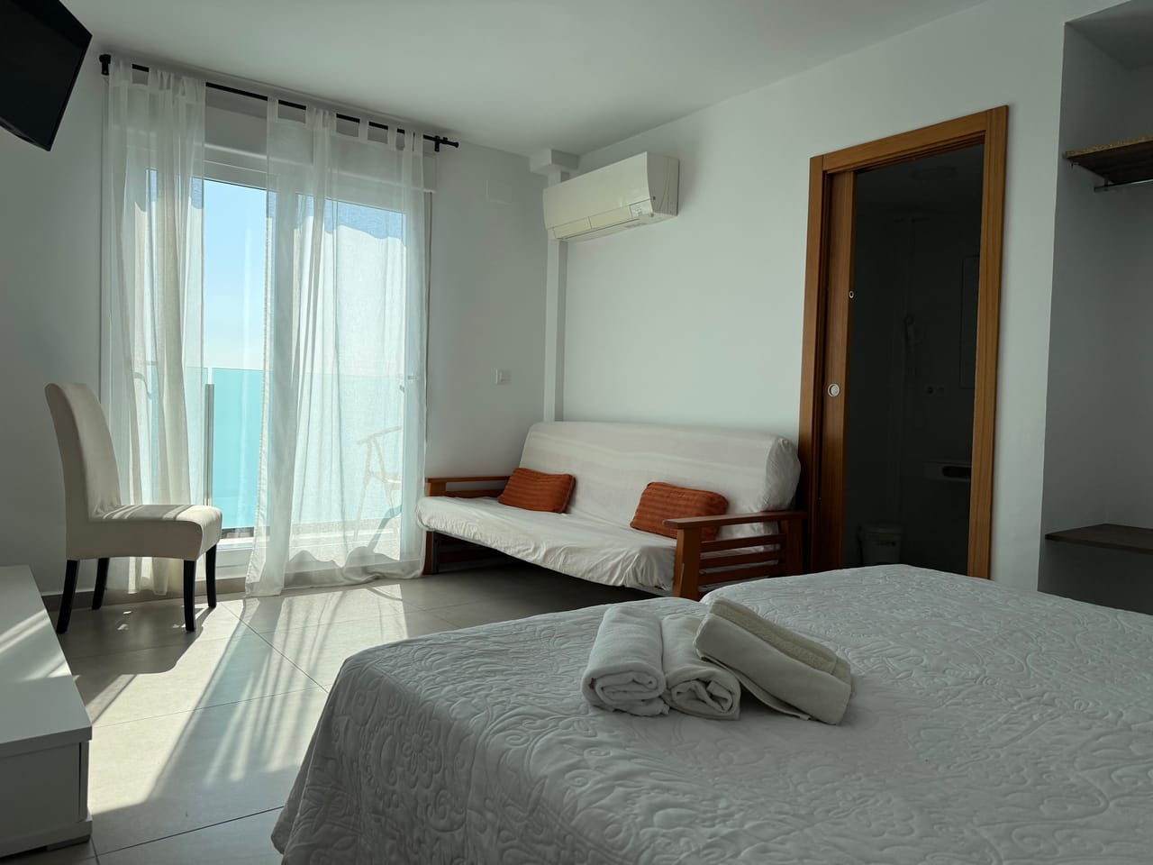 Habitación amplia con sofá y cojines en tono teja, mar al fondo