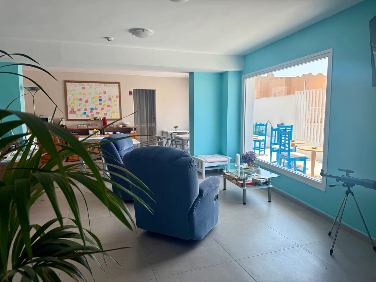 Sala común de Living One con sillón azul, plantas y un gran ventanal a la terraza