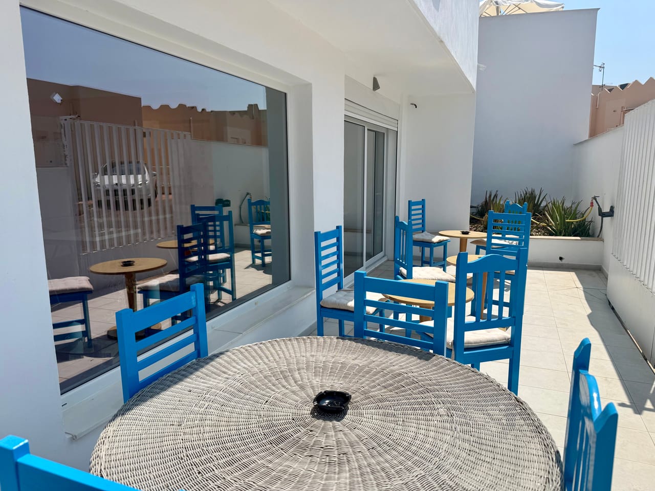 Terraza con sillas azules mediterráneas y mesa de mimbre bajo el sol